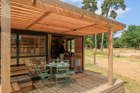 Houten terras bij Chalet Evasion met tuinset, omgeven door natuur en iemand in het chalet binnen.