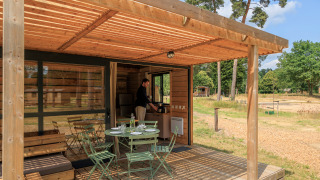 Houten terras bij Chalet Evasion met tuinset, omgeven door natuur en iemand in het chalet binnen.