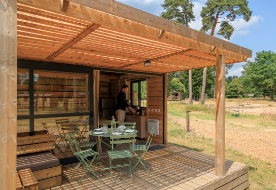 Terraza de madera en Chalet Evasion con mesa y sillas, rodeada de naturaleza y una persona adentro.