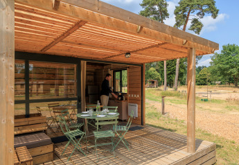 Terraza de madera en Chalet Evasion con mesa y sillas, rodeada de naturaleza y una persona adentro.