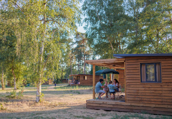 Familie nyder udendørs ophold ved Chalet Evasion i Huttopia De Meinweg, omgivet af træer og natur.