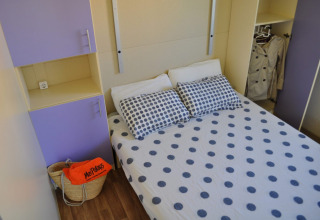 Chambre du Bungalow Morea au Camping Mas Patoxas en Espagne avec lit double et armoires violettes.