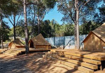 Glamping Nature Tent en Camping Mas Patoxas, España, con grandes tiendas tipi sobre terrazas de madera y árboles.