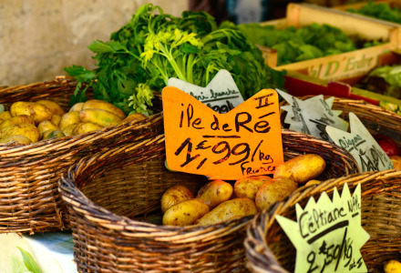 Patatas frescas y verduras en cestas de mimbre con coloridos carteles de precios en un mercado cerca de Courtils, Normandía.