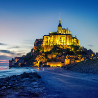 Vista del Mont Saint-Michel iluminado al anochecer cerca de Courtils, Normandía, Francia, reflejado sobre la marea baja.
