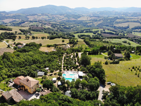 Aerial view of Camping Casa Tartufo holiday park in Marche, Italy, surrounded by lush hills and fields.