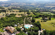 Luftfoto af Camping Casa Tartufo feriepark i Marche, Italien, omgivet af grønne bakker og landskab.