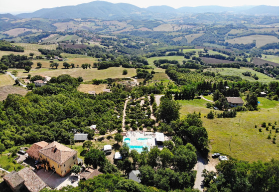 Luchtfoto van Camping Casa Tartufo vakantiepark in Marche, Italië, omgeven door groene heuvels en velden.