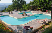 Swimmingpool med træterrasse og liggestole på Camping Casa Tartufo, omgivet af grøn natur i Marche, Italien.