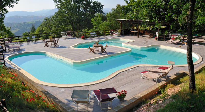 Buitenzwembad met ligstoelen op Camping Casa Tartufo, gelegen in het groene landschap van Marche, Italië.