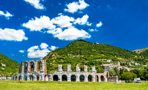 Ruinas de un antiguo anfiteatro romano entre colinas verdes cerca de Sassoferrato, Marche, Italia, bajo un cielo azul.