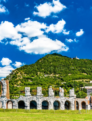 Ruinas de un antiguo anfiteatro romano entre colinas verdes cerca de Sassoferrato, Marche, Italia, bajo un cielo azul.