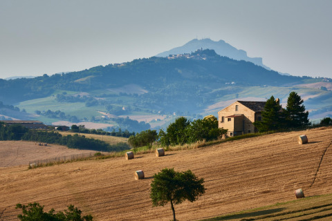 Glooiende velden nabij Sassoferrato, Marche, Italië, met hoeve en ronde hooibalen op gouden akkers.