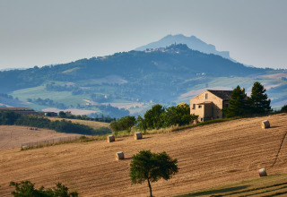 Glooiende velden nabij Sassoferrato, Marche, Italië, met hoeve en ronde hooibalen op gouden akkers.