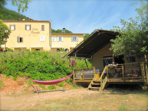 Safari-tent Wood Lodge met hangmat en bloemen bij Camping Casa Tartufo in Italië, omgeven door groen.