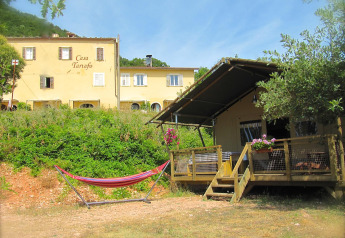 Tienda safari Wood Lodge con hamaca y flores en Camping Casa Tartufo en Italia, rodeada de naturaleza.