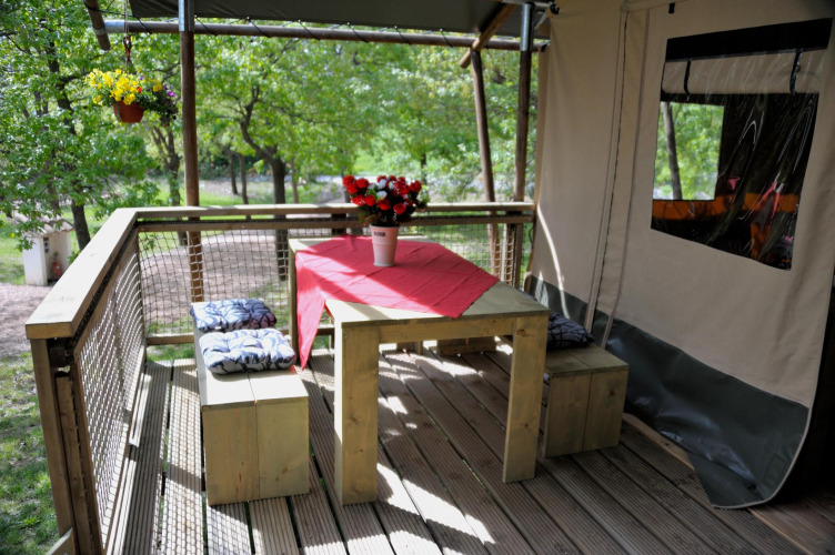 Holzterrasse mit Esstisch und Bänken am Wood Lodge Safari-Zelt auf Camping Casa Tartufo in Italien.