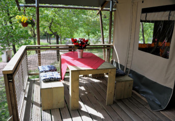 Holzterrasse mit Esstisch und Bänken am Wood Lodge Safari-Zelt auf Camping Casa Tartufo in Italien.