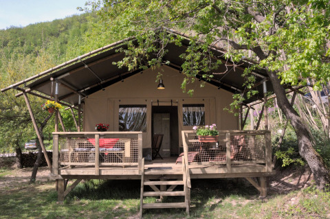 Safari-tent Wood Lodge bij Camping Casa Tartufo in Italië met houten terras in groene, bosrijke omgeving.