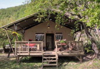 The Wood Lodge safari tent at Camping Casa Tartufo in Italy, featuring a wooden deck surrounded by trees.