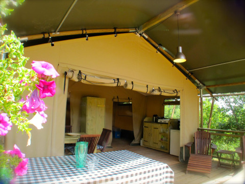 Escena al aire libre en la tienda safari Wood Lodge de Camping Casa Tartufo en Italia, con flores y mesa.