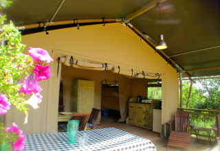 Escena al aire libre en la tienda safari Wood Lodge de Camping Casa Tartufo en Italia, con flores y mesa.