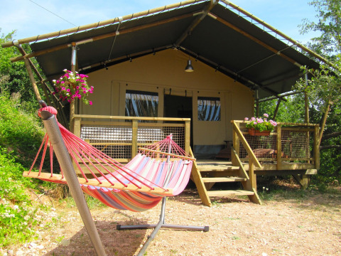 Vista exterior de una tienda safari llamada Wood Lodge con hamaca colorida y flores en la terraza de madera.