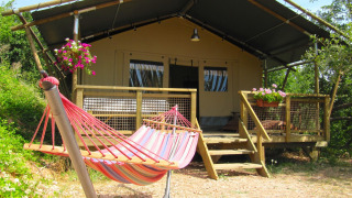 Vista esterna di una tenda safari chiamata Wood Lodge con amaca colorata e fiori sulla veranda in legno.