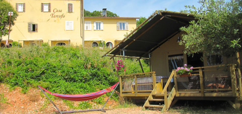 Blokhut, hangmat en hoofdgebouw bij Camping Casa Tartufo vakantiepark in Marche, Italië.