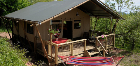 A glamping tent with a porch and hammock surrounded by greenery at Camping Casa Tartufo in Marche, Italy.