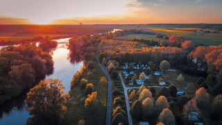 Vista aérea de Camping Seasonova Le Martinet al atardecer, con río, cabañas y árboles otoñales en Francia.