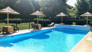 Piscina al aire libre con sombrillas de paja y tumbonas en Camping Seasonova Le Martinet, Centre-Val de Loire, Francia.