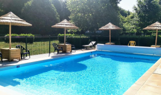 Outdoor pool with straw umbrellas, sun loungers, and greenery at Camping Seasonova Le Martinet, France.