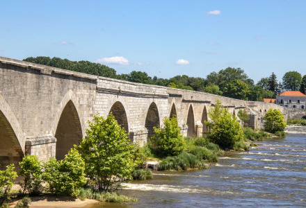 Puente de piedra histórico sobre un río cerca de Briare-le-Canal, rodeado de vegetación y árboles.