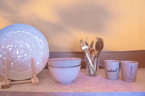 Ceramic plate, bowls, cutlery in a glass, and cups on a shelf at Little Canvas Escape, Friesland, Netherlands.