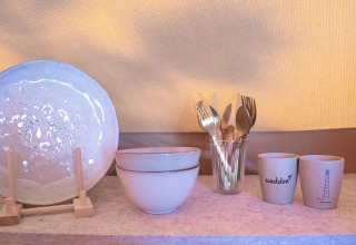 Ceramic plate, bowls, cutlery in a glass, and cups on a shelf at Little Canvas Escape, Friesland, Netherlands.
