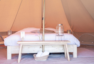 Interieur van een luxe tent met tweepersoonsbed, houten bankje en decoratie in Friesland, Nederland.