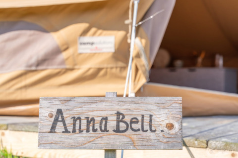 Cartel de madera con 'Anna Bell.' frente a una tienda glamping en Little Canvas Escape, Friesland, Países Bajos.