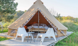 Luxuszelt mit zwei weißen Stühlen auf Holzterrasse im Little Canvas Escape, Friesland, Niederlande.