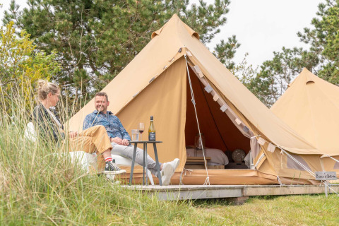 Zwei Personen entspannen sich vor einem luxuriösen Zelt im Little Canvas Escape Ferienpark in Friesland, Niederlande.