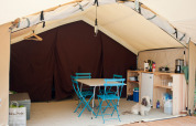 Innenraum eines Safari-Bungalowzeltes mit blauen Stühlen, Tisch, Küchenzeile und Hund.