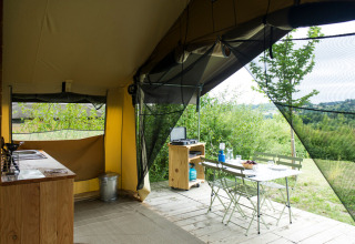 Vista interior de una tienda safari con muebles de madera y vista a la naturaleza en Huttopia La Plage Blanche.
