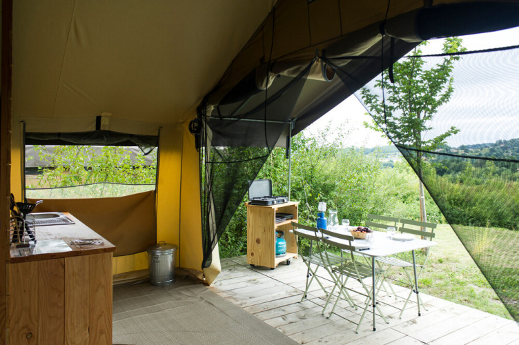 Vista interior de una tienda safari con muebles de madera y vista a la naturaleza en Huttopia La Plage Blanche.