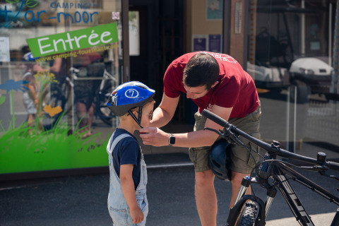 Un adulto aiuta un bambino con il casco da bici fuori dal Camping Kost Ar Moor in Bretagna, Francia.