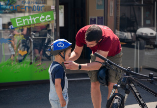 Un adulto ayuda a un niño con el casco de bicicleta frente a Camping Kost Ar Moor en Bretaña, Francia.