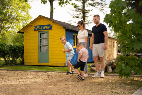 Gezin speelt petanque voor het gele clubhuis op Camping Kost Ar Moor, een vakantiepark in Bretagne, Frankrijk.