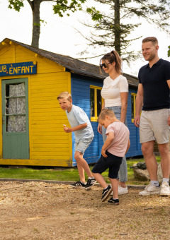 Familia jugando petanca frente a la caseta amarilla en Camping Kost Ar Moor, un parque vacacional en Bretaña.
