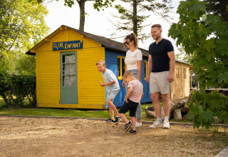 Gezin speelt petanque voor het gele clubhuis op Camping Kost Ar Moor, een vakantiepark in Bretagne, Frankrijk.
