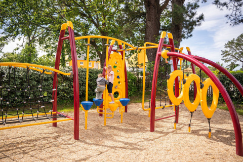 Parco giochi con struttura colorata e bambini, punto forte del Camping Kost Ar Moor in Bretagna, Francia.