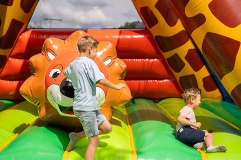 Twee kinderen amuseren zich op een kleurrijk springkasteel met leeuw bij Camping Kost Ar Moor, Bretagne.